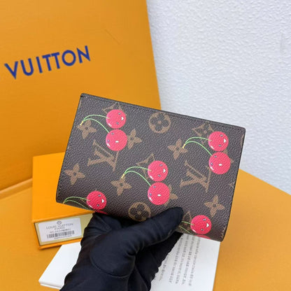 Louis Vuitton wallet with cherry design held by a gloved hand against a Vuitton box background.